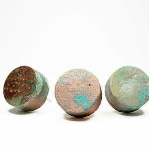 May include: Three round, decorative knobs with a textured surface. The knobs are painted in shades of brown, pink, and green.