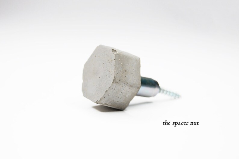 May include: A concrete hexagon-shaped hook with a silver metal screw. The hook is attached to a wall with a screw. The text "the spacer nut" is visible below the hook.