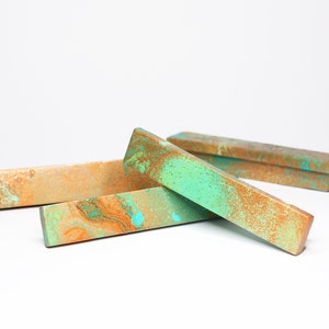 May include: Three rectangular drawer pulls with a marbled finish in shades of gold, green, and turquoise.