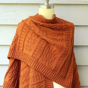 Może przedstawiać: Rdzawy, dzianinowy szal z wzorem warkoczowym. Szal jest zarzucony na biały manekin.