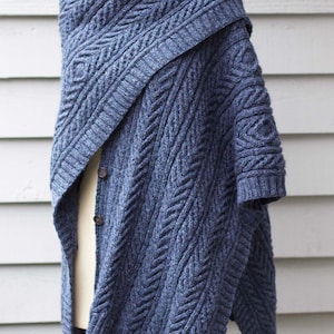 May include: A blue knitted cardigan with a cable knit pattern. The cardigan has a shawl collar and is draped over a dress form.
