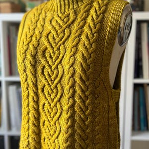 Peut inclure: Un pull en maille jaune sans manches avec un motif en câble.