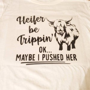 K&ouml;nnte beinhalten: Wei&szlig;es T-Shirt mit einer schwarzen Grafik einer Highland-Kuh und dem Text "Heifer be trippin' OK... MAYBE I PUSHED HER"