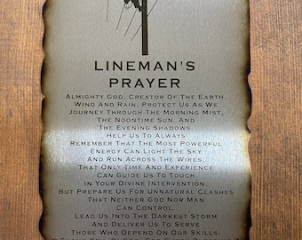 May include: A metal sign with a burnt edge and a distressed look. The sign features a silhouette of a lineman working on a power line. The text on the sign reads "Lineman's Prayer" and includes a prayer for safety and guidance.