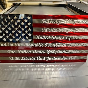 May include: A metal American flag with the Pledge of Allegiance engraved on it. The flag is red, white, and blue with a wavy, textured surface.