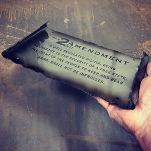 May include: A metal sign with a distressed, burnt look, featuring the text "The 2nd Amendment" and the full text of the Second Amendment to the United States Constitution.