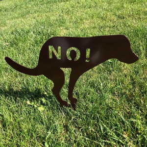 May include: A black metal silhouette of a dog in a squatting position with the word "NO!" cut out of the silhouette. The silhouette is on a green grassy lawn.