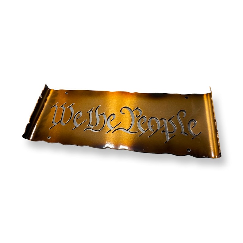 Peut inclure: Une plaque en m&eacute;tal dor&eacute; avec les mots "We the People" d&eacute;coup&eacute;s dans une police d'&eacute;criture cursive. La plaque a un aspect vieilli et us&eacute;.