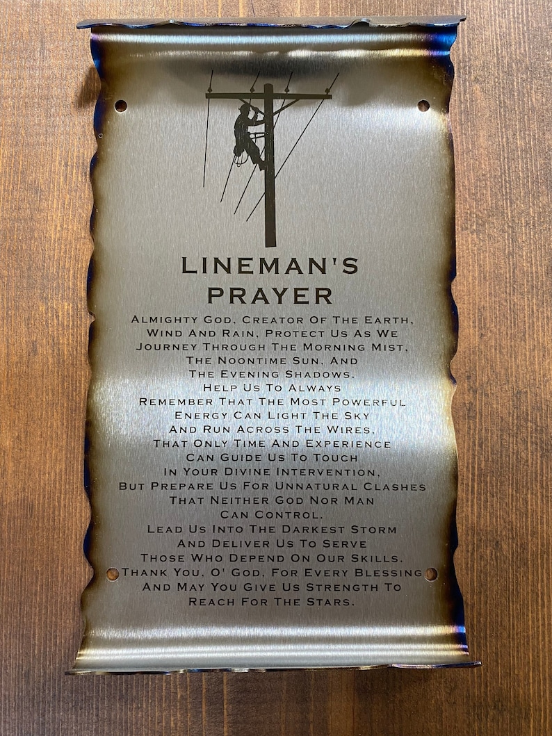May include: A metal sign with a burnt edge and a distressed look. The sign features a silhouette of a lineman working on a power line. The text on the sign reads "Lineman's Prayer" and includes a prayer for safety and guidance.