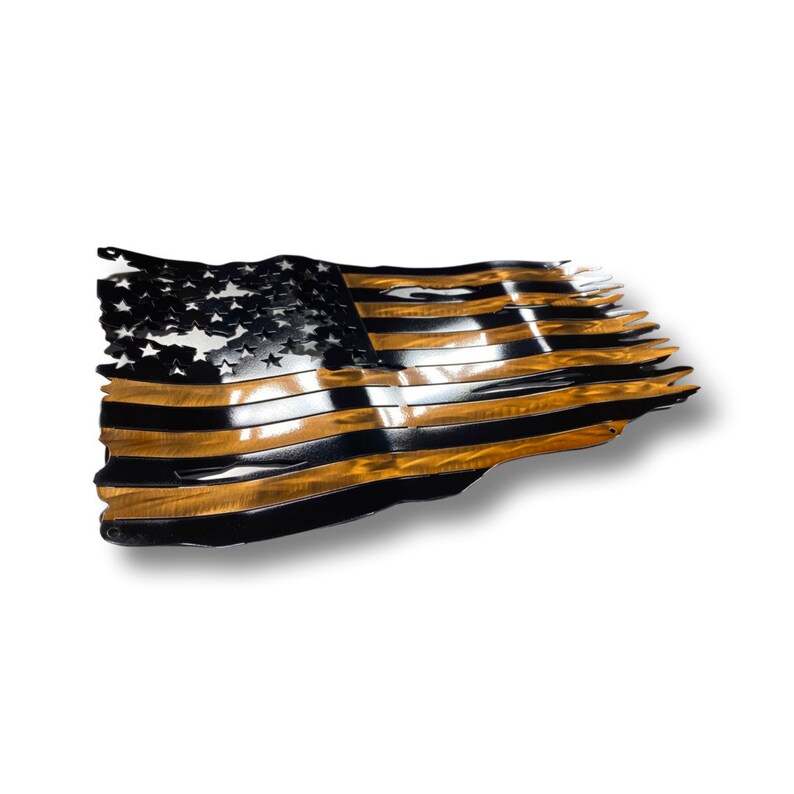 May include: Metal American flag wall art. The flag features a distressed design with black and gold stripes and stars. The flag appears to be waving, with the edges torn and tattered. The artwork is mounted on a white background.