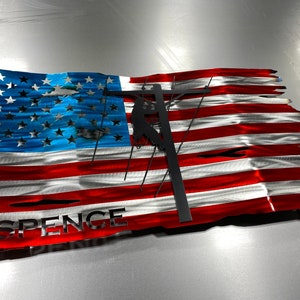 May include: A distressed metal American flag with a silhouette of a lineman working on a power pole. The flag is red, white, and blue with the name "SPENCE" at the bottom.