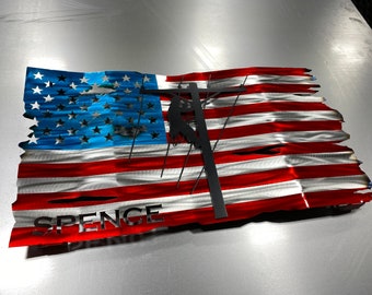 May include: A distressed metal American flag with a silhouette of a lineman working on a power pole. The flag is red, white, and blue with the name "SPENCE" at the bottom.