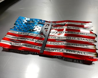 May include: A metal American flag wall art with a silhouette of a lineman working on a power line. The flag is distressed and has the words "And to the Republic for which it stands, One Nation under God, indivisible, with liberty and justice for all." printed on it.
