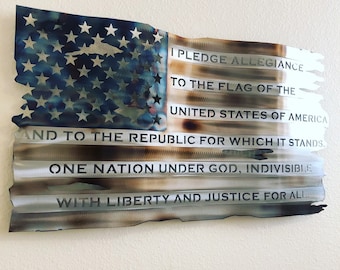 May include: Metal wall art depicting the American flag, with the Pledge of Allegiance inscribed. The flag design includes a blue section with stars and red and white stripes, with a distressed finish.