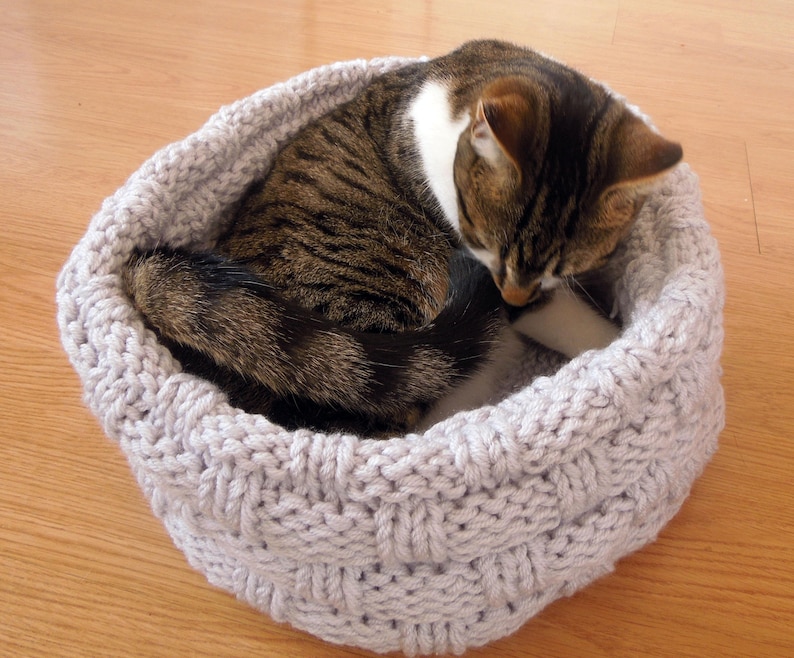 May include: A gray knitted cat bed with a tabby cat curled up inside. The cat bed is made of a soft, cozy material and is perfect for a cat to relax and sleep in.