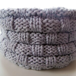 May include: A gray knitted basket with a woven pattern. The basket is made of thick yarn and has a round shape.