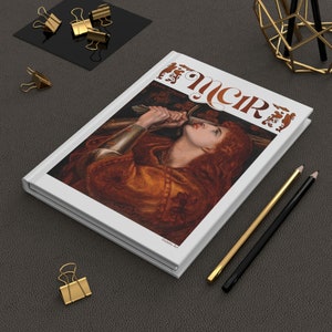 以下が含まれることがあります： スタイリッシュなフォントで「The Circe」というタイトルが書かれた白いハードカバーの本。表紙には、剣を持った赤い髪の女性が空を見上げている絵が描かれている。本は、灰色の表面に金のクリップと鉛筆が置かれている。