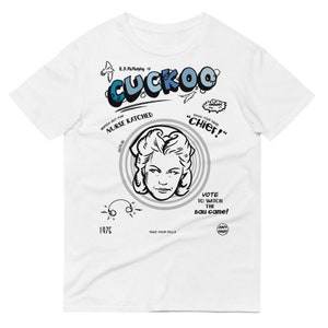 May include: White t-shirt with a black and white illustration of a woman with a nurse's cap. The text "CUCKOO" is in blue and white letters. The text "WATCH OUT FOR NURSE RATCHED" is in black and white letters. The text "CAUSE YOUR HAND "CHIEF!" is in black and white letters. The text "VOTE TO WATCH THE BALL GAME!" is in black and white letters. The text "1975" is in black and white letters. The text "TAKE YOUR PILLS" is in black and white letters.