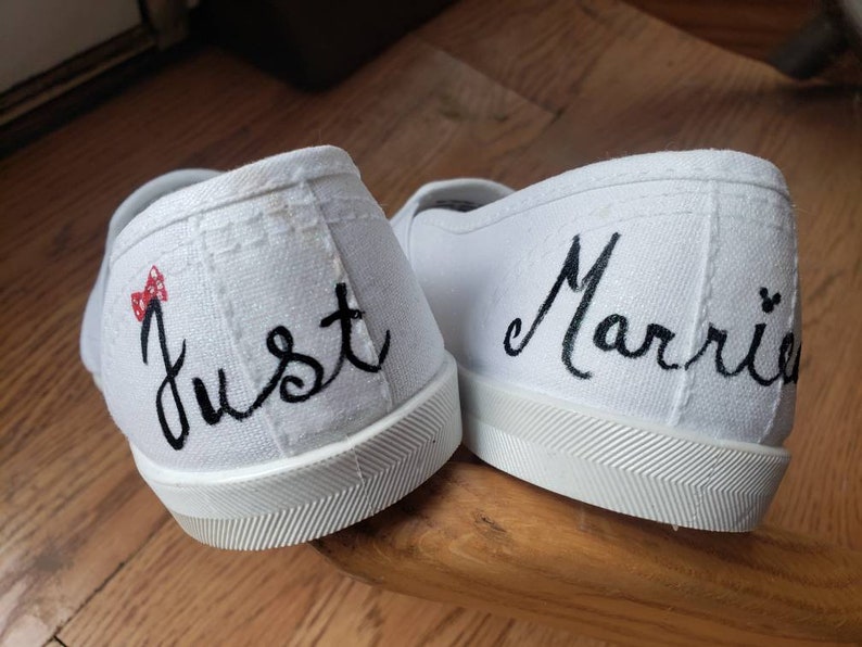 May include: A pair of white canvas shoes with black embroidery. One shoe says "Just" with a red and white polka dot bow. The other shoe says "Married" with a Mickey Mouse silhouette.