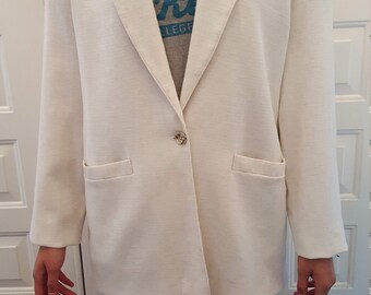 May include: A cream-colored blazer with a single button closure and two front pockets. The blazer is worn over a gray v-neck t-shirt with the text "Bucks College". The person is wearing maroon leggings.