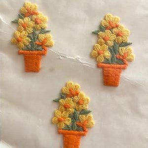 May include: Vintage package of E-3 Schiffli Motifs appliques. The package features three embroidered flower pot appliques with yellow flowers and green leaves. The package text reads "Adds Fashion and Style with Appliques".