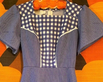 May include: A blue and white gingham dress with short sleeves and two patch pockets. The dress has a white trim around the neckline, sleeves, and pockets.