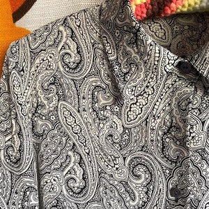 May include: A white shirt with a black paisley pattern. The shirt has a button-up collar and long sleeves.