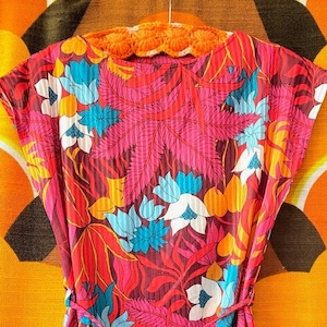 May include: A pink, orange, blue, and white floral print top with a tie at the waist. The top has short sleeves and a scoop neck.