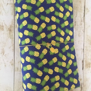 May include: A blue fabric notebook cover with a repeating pattern of yellow pineapples on a dark blue background. The cover has a gold zipper and a gold pineapple charm.