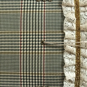 May include: A brown and green plaid fabric journal with a white lace trim and gold ribbon. The journal has metal eyelets and a brown string closure.
