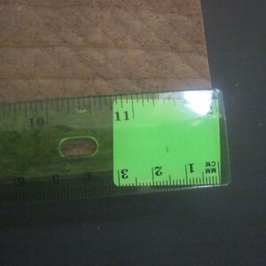 May include: A green ruler with black markings, showing measurements in inches and centimeters. The ruler is placed on a brown surface.