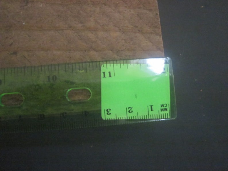 May include: A green ruler with black markings, showing measurements in inches and centimeters. The ruler is placed on a brown surface.