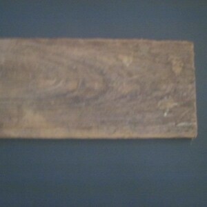 May include: A close-up of a piece of wood with a natural wood grain pattern. The wood is a light brown color with some darker brown streaks.