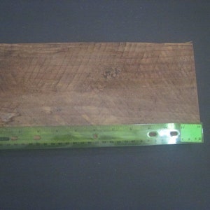 May include: A close-up of a piece of wood with a natural wood grain pattern. A green ruler is placed below the wood, measuring 12 inches.