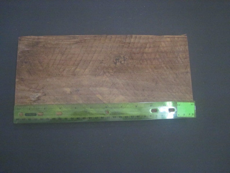 May include: A close-up of a piece of wood with a natural wood grain pattern. A green ruler is placed below the wood, measuring 12 inches.