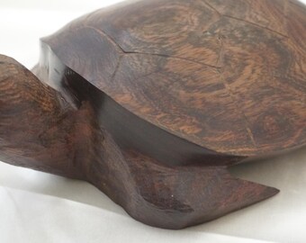 May include: A handcrafted wooden turtle sculpture. The turtle is carved from dark brown wood, showcasing the natural grain patterns. The head and flippers are extended, giving the impression of movement. A decorative item.