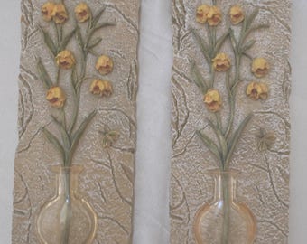 May include: A pair of rectangular wall plaques featuring a textured beige stone-like background. Each plaque displays a relief of yellow flowers in a clear glass vase with green stems and leaves, accompanied by a small sculpted butterfly detail.