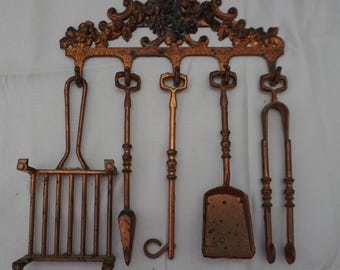 May include: A vintage copper-toned fireplace tool set. The set includes a rack, poker, shovel, tongs, and a tool with a curved handle. The tools hang from a decorative floral-patterned wall mount. The set is made of metal.