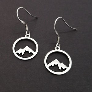 May include: A pair of silver earrings with a mountain silhouette design. The earrings are circular and have a simple, minimalist style.