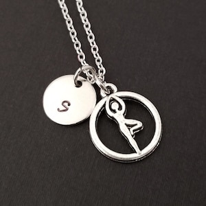 May include: Silver necklace with a round pendant featuring a yoga pose silhouette and a smaller round pendant with the letter 'S' engraved on it.