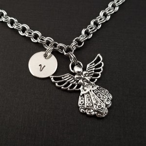 Peut inclure: Un collier en cha&icirc;ne argent avec un pendentif ange en argent et un pendentif rond en argent grav&eacute; de la lettre "V".