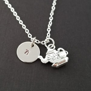 May include: Silver necklace with a small teapot charm and a round pendant with the letter "N" engraved on it.