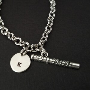 May include: A silver chain bracelet with a charm of a flute and a round charm with the letter K.
