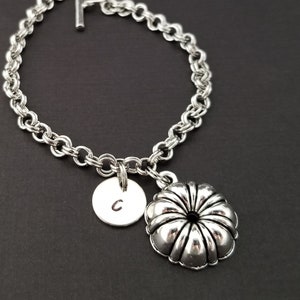 May include: A silver chain bracelet with a silver charm in the shape of a flower and a silver disc charm with the letter C engraved on it.