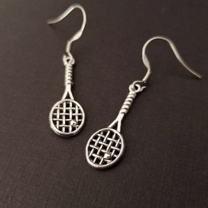 May include: A pair of silver tennis racket earrings. Each earring features a detailed tennis racket with a small ball at the center of the racket.