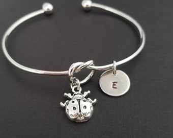 Puede incluir: Pulsera de plata con cierre de nudo, un dije de mariquita y un dije redondo con la letra 'E' grabada.
