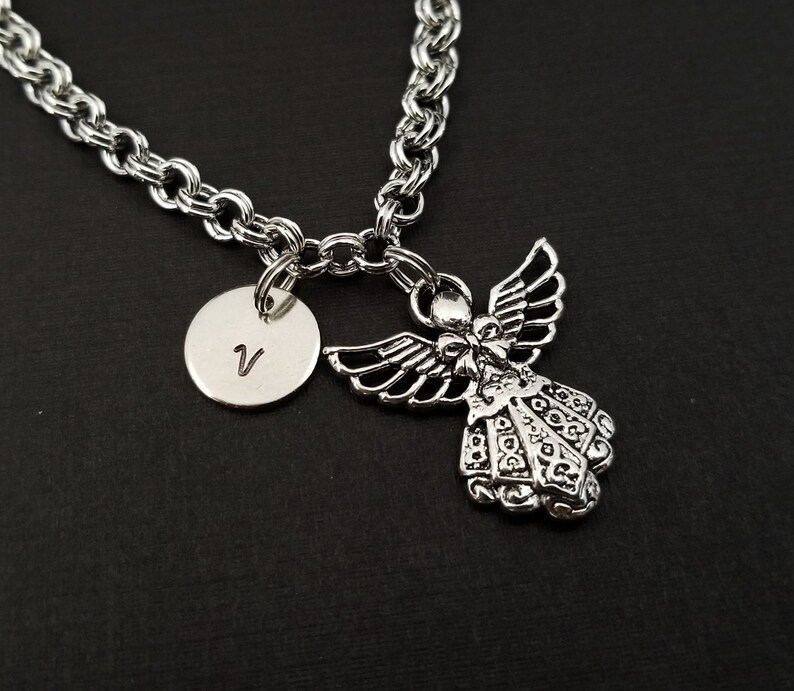 Peut inclure: Un collier en cha&icirc;ne argent avec un pendentif ange en argent et un pendentif rond en argent grav&eacute; de la lettre V.