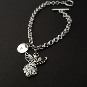 Peut inclure: Bracelet en cha&icirc;ne argent avec un charme ange en argent et un charme disque en argent avec la lettre "V" grav&eacute;e dessus.