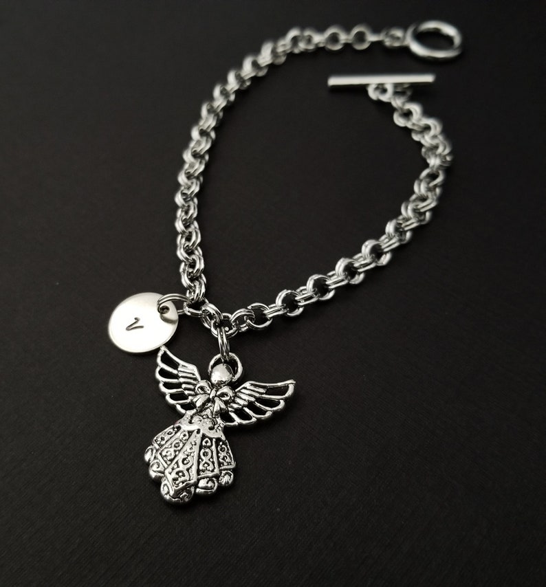 Peut inclure: Bracelet en cha&icirc;ne argent avec un charme ange en argent et un charme disque en argent avec la lettre "V" grav&eacute;e dessus.
