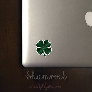 May include: A green shamrock sticker with a plaid pattern on a silver laptop. The sticker has a yellow outline and is placed on the top right corner of the laptop.